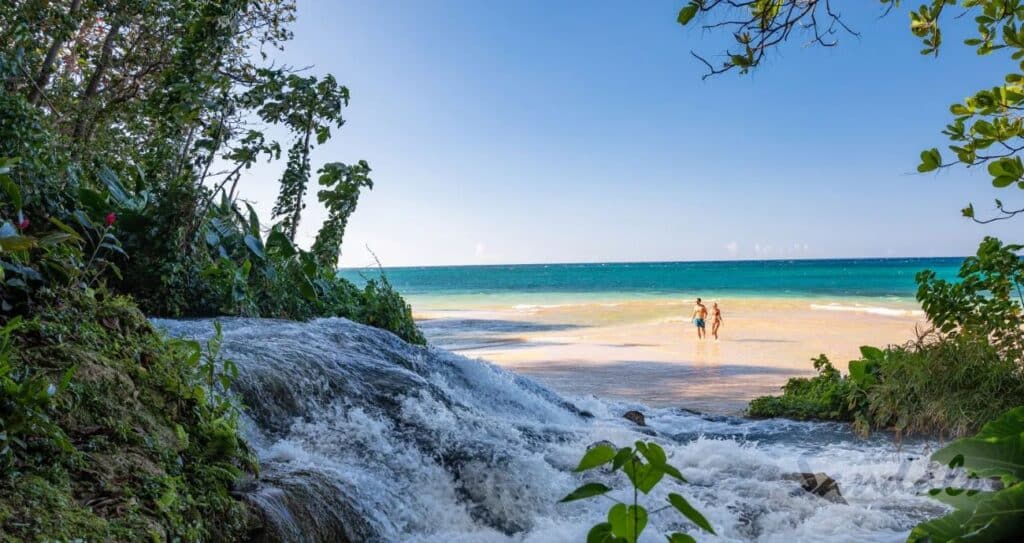 river flowing on to a beach where two people are walking